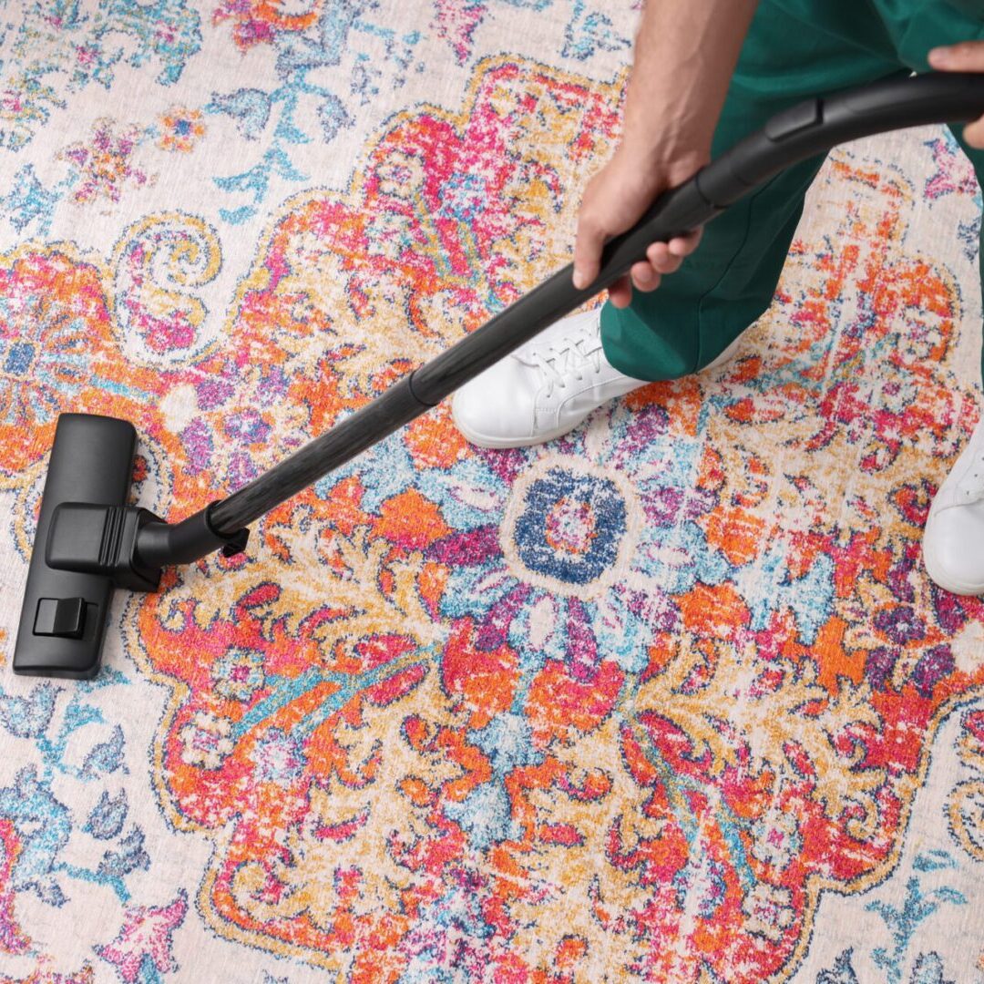 Person vacuuming colorful patterned rug.