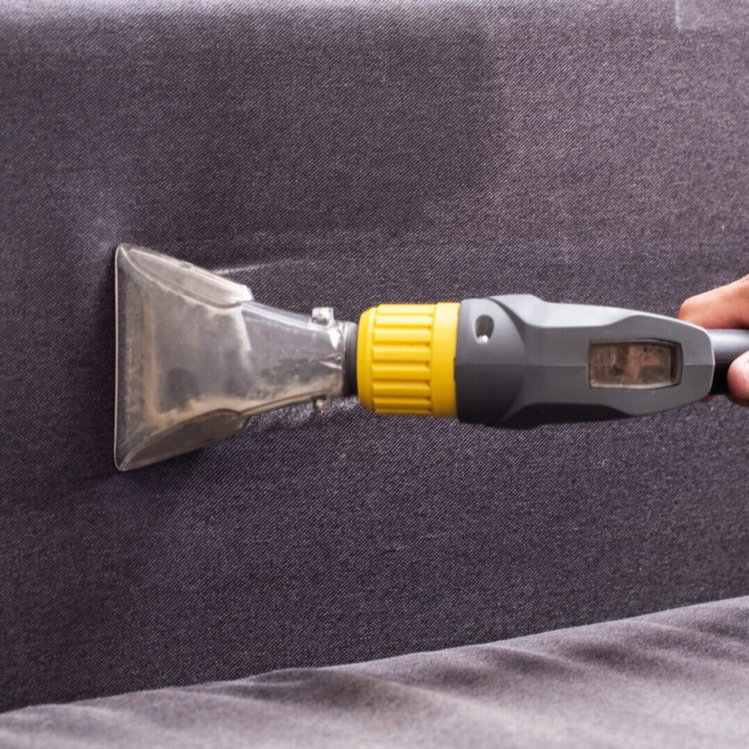Dry cleaning of the black upholstery on the sofa with a special washing vacuum cleaner. Copy space for text Vacuum cleaning a grey upholstered sofa.